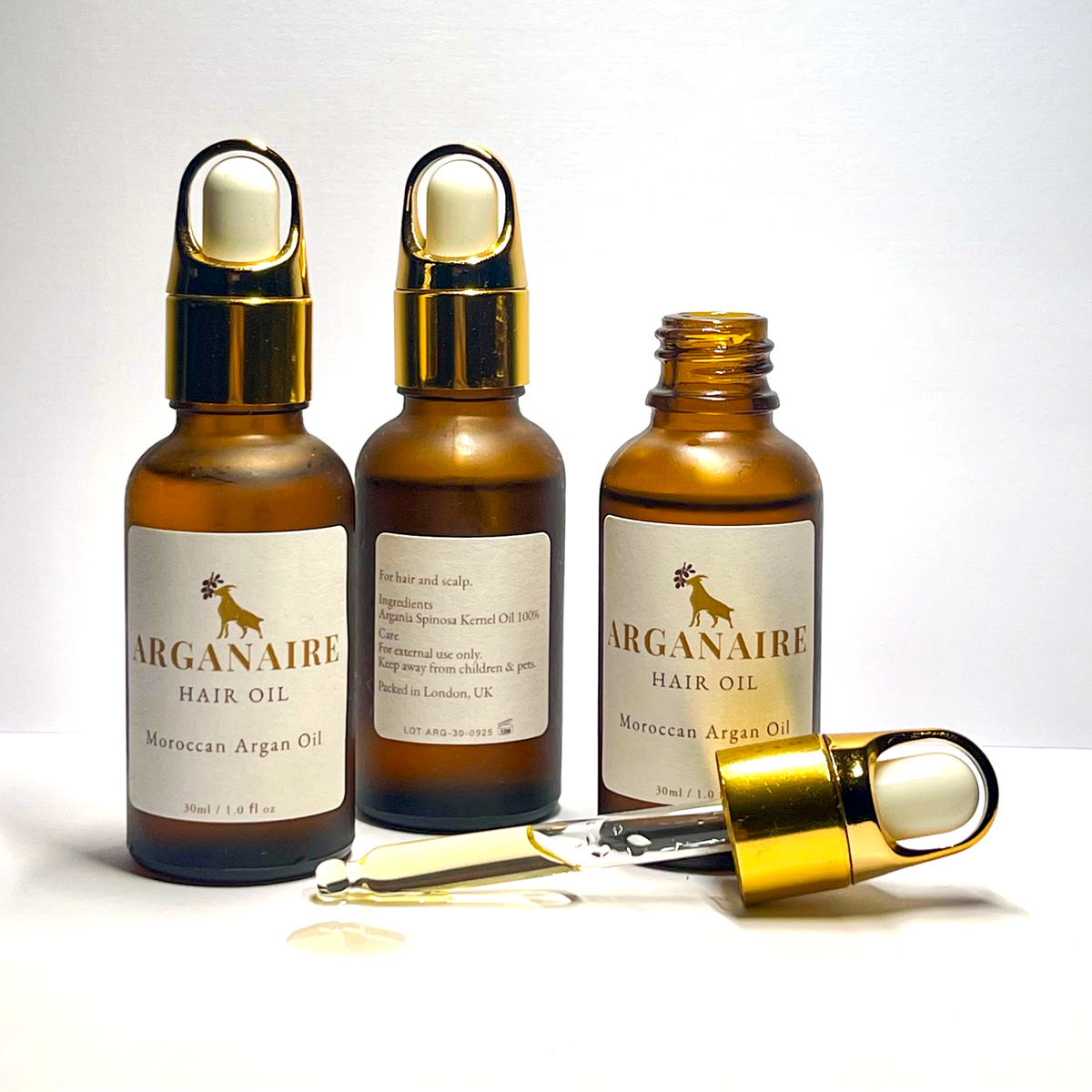 Three authentic 30 ml Arganaire bottles showing front and ingredient labels with an open glass dropper and golden argan oil